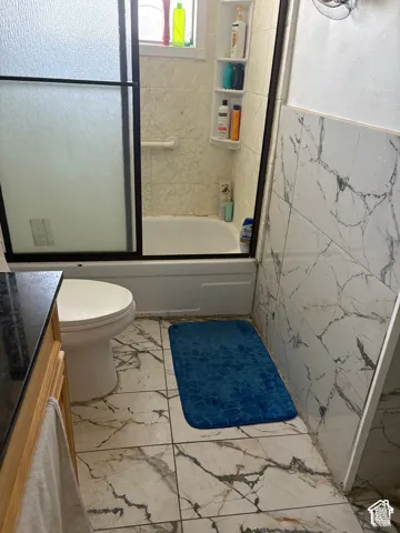Bathtub with sliding shower doors, white subway tile surround, built-in shelving, and marble-look floor tiling