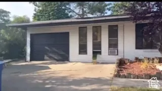 White horizontal siding exterior with a dark garage door, multiple windows, and an established front yard planting area