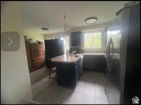 Kitchen featuring an island with counter seating, stainless steel refrigerator, white tile flooring, recessed lighting, and a window above the sink