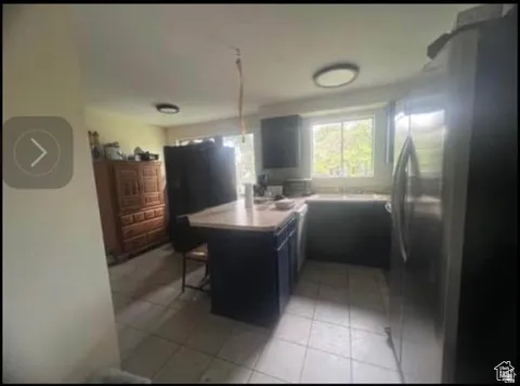Kitchen featuring an island with counter seating, stainless steel refrigerator, white tile flooring, recessed lighting, and a window above the sink
