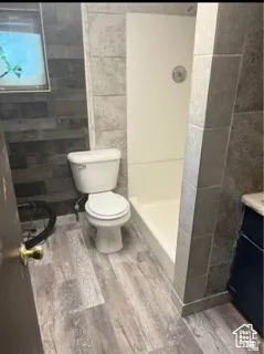 Walk-in shower with tile surround, wood-finish flooring, and a white toilet