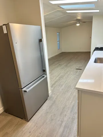 Stainless steel refrigerator, wood-finish flooring, white countertops, built-in ceiling lighting, and a ceiling fan