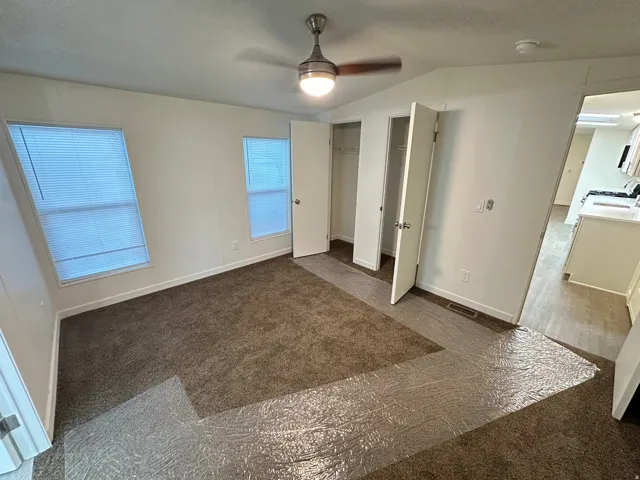 White walls with two windows featuring blinds, brown carpet flooring, and a ceiling fan with light fixture