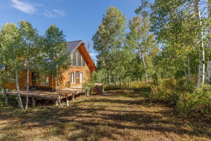 Log cabin exterior with a large wood deck, a metal roof, and abundant surrounding trees