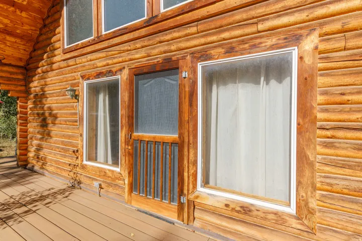 Log cabin exterior with an expansive wood deck, wood-framed windows, and a wood screen door