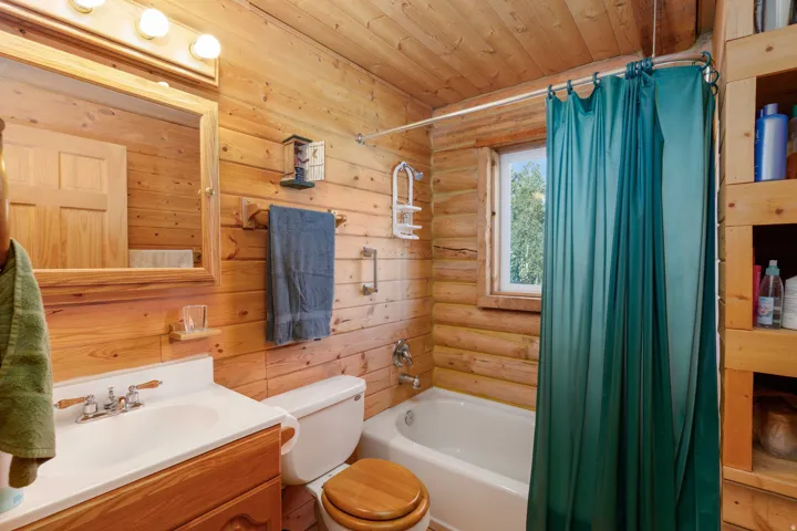 Wood-paneled bathroom featuring a built-in vanity with integrated sink, a full bathtub with shower, wood-framed mirror, and integrated shelving