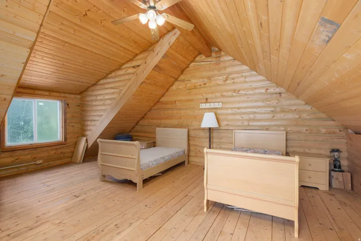 Wood-paneled sloped ceiling, wood-plank flooring, log wall construction, exposed wood beam, and a ceiling fan with light fixture