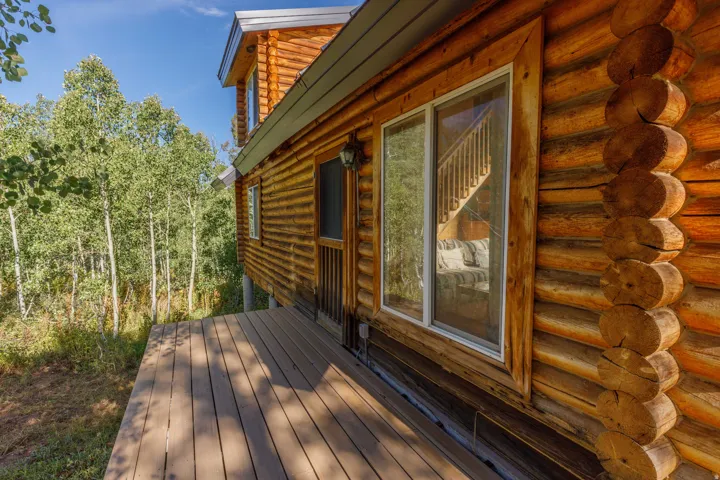 Log cabin exterior with a composite deck, surrounded by mature trees