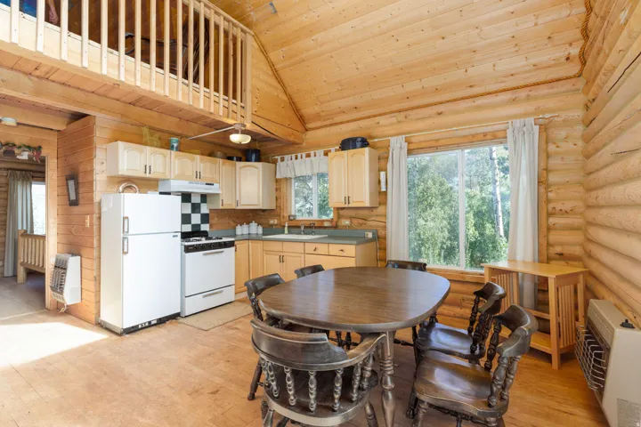 Log cabin interior featuring wood-finish flooring, a kitchen with light wood cabinetry, a checkerboard backsplash, and a loft space with wood railing