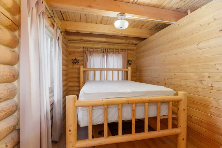 Interior featuring log walls, wood-paneled ceiling, wood-finish flooring, and a window with sheer curtains