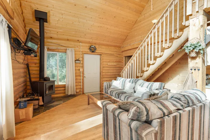 Vaulted wood-paneled ceilings, wood-finish flooring, log wall construction, a built-in wood-burning stove, and a wood staircase with balusters