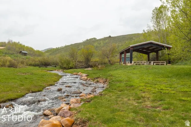 Expansive green space featuring a natural stream, a covered pavilion with built-in picnic tables, and a distant outbuilding