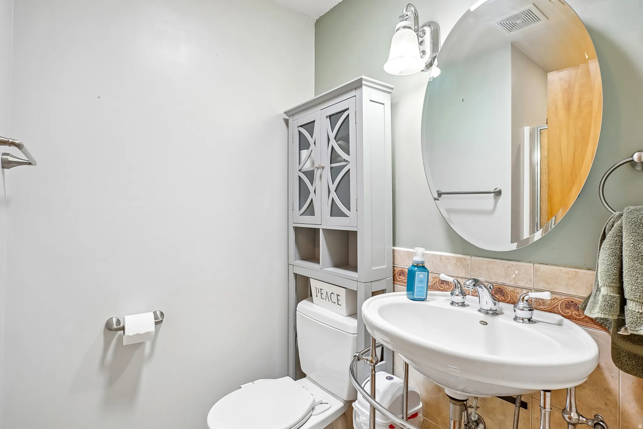 Pedestal sink with chrome fixtures and an oval mirror