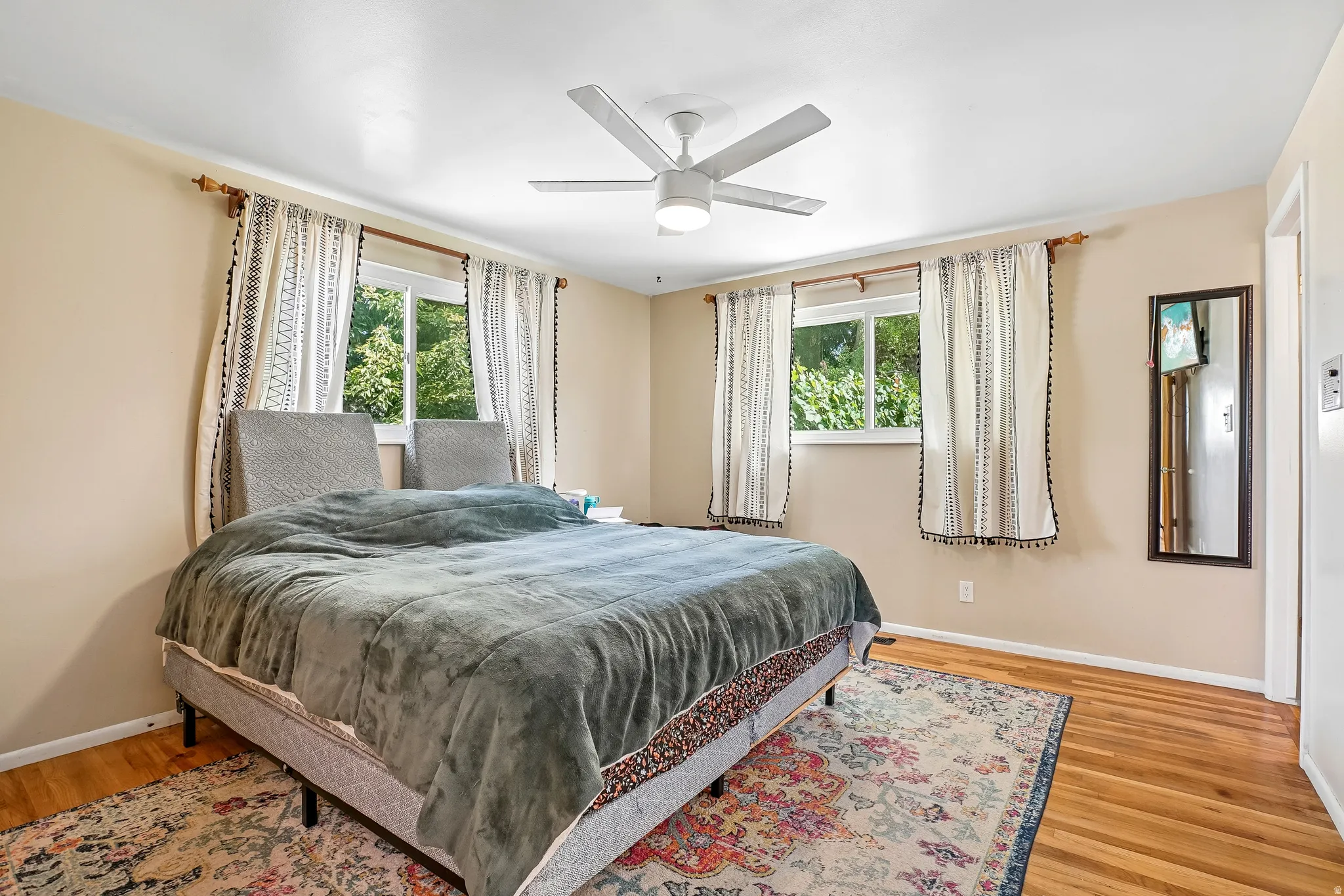 Hardwood flooring, two windows, ceiling fan, neutral wall tones, and white trim