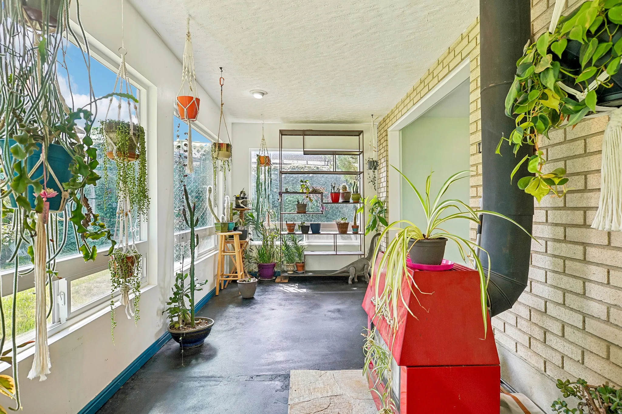 Enclosed sunroom featuring multiple large windows, a light-colored brick wall, and a dark-colored concrete floor