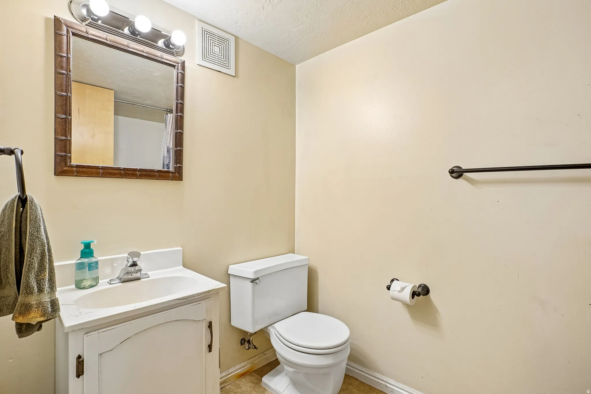 Vanity with integrated sink, wall-mounted mirror, overhead vanity lighting, toilet, and towel bar