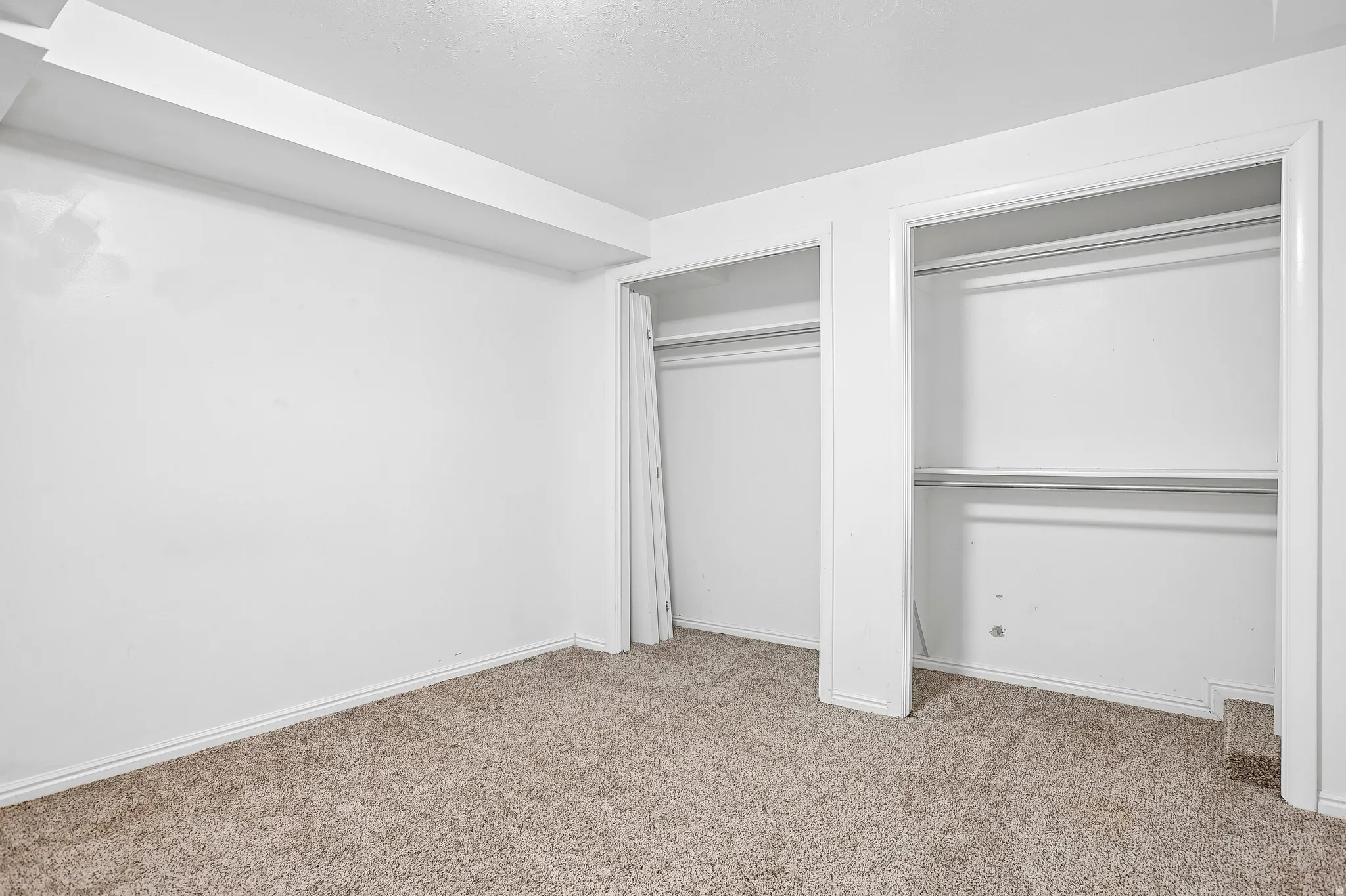 White walls with carpet flooring, featuring two closet openings with hanging rods and built-in shelving