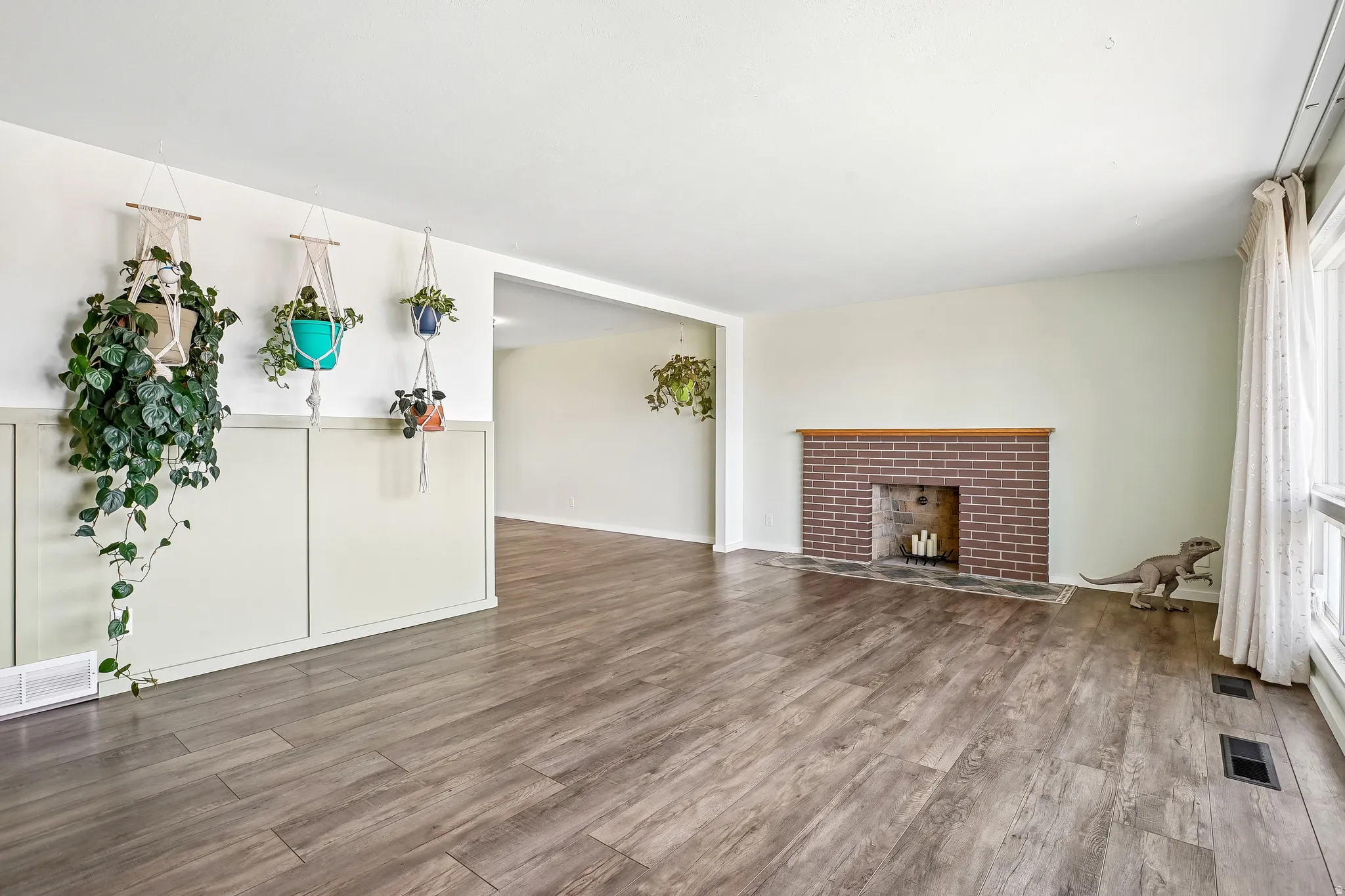 Wood-finish flooring, half-wall paneling, brick fireplace with a wood mantel, and large window