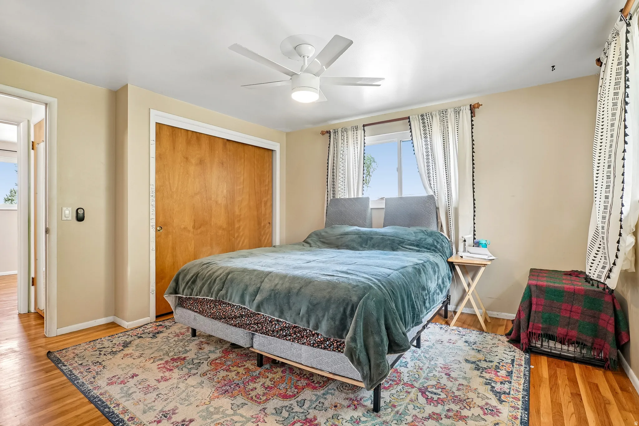 Hardwood flooring, wood-finish bi-fold closet doors, ceiling fan with integrated lighting, and multiple windows