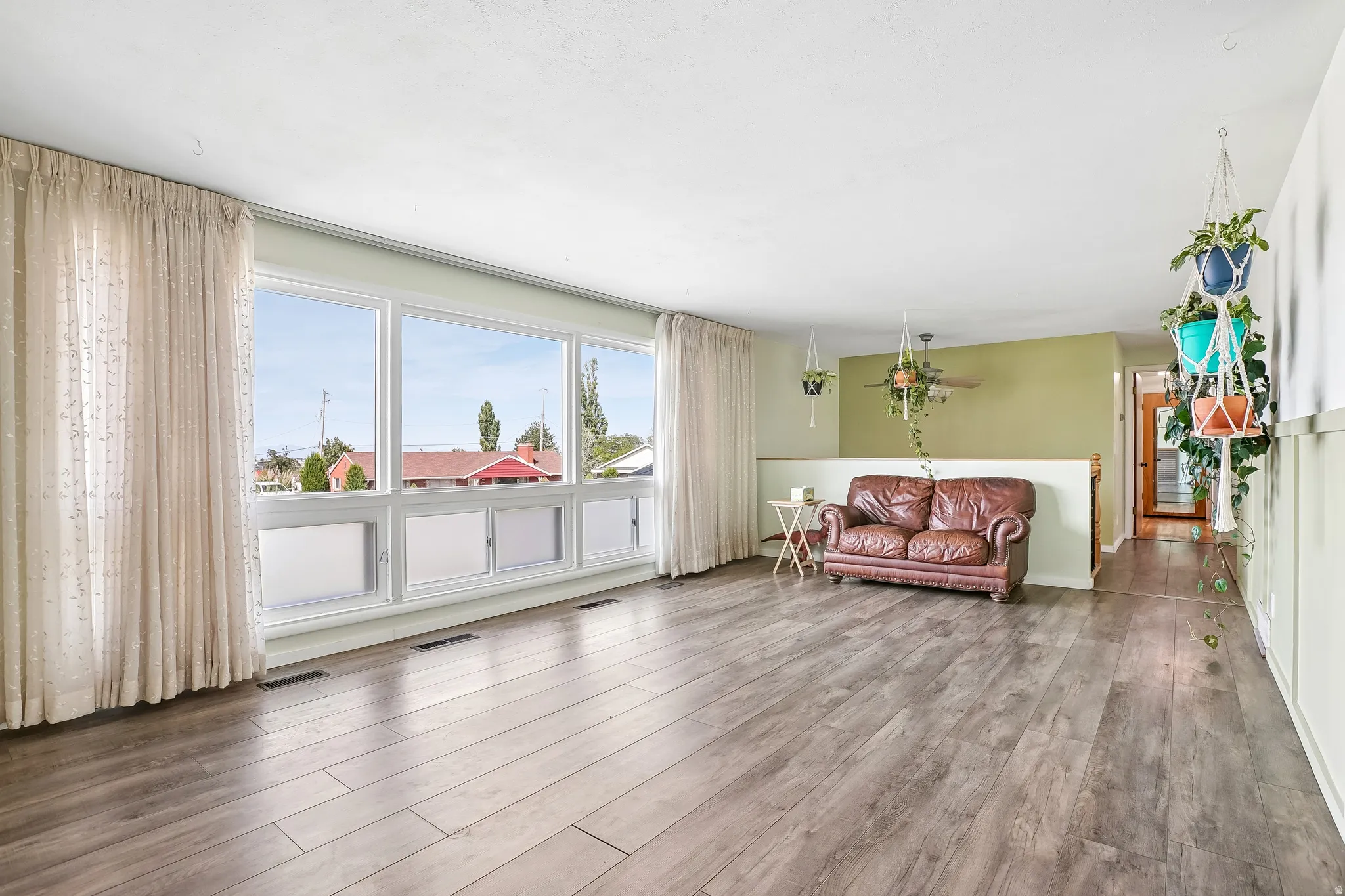 Expansive room featuring wood-finish flooring, a large multi-pane window, and a partial wall with a half-height partition