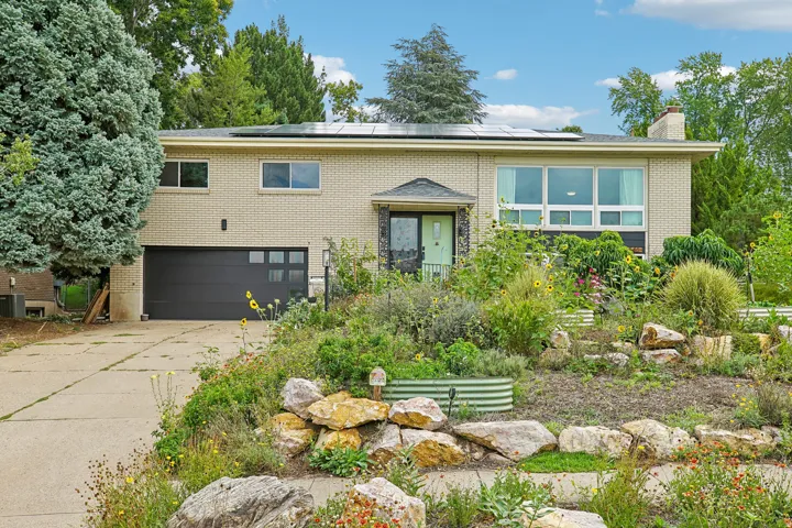 Brick exterior featuring a dark garage door, solar panels, and extensive front landscaping with rock elements
