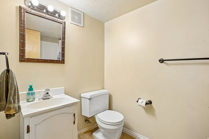 Vanity with integrated sink, wall-mounted mirror, overhead vanity lighting, toilet, and towel bar