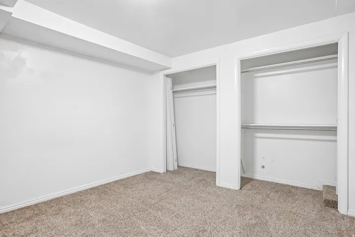 White walls with carpet flooring, featuring two closet openings with hanging rods and built-in shelving