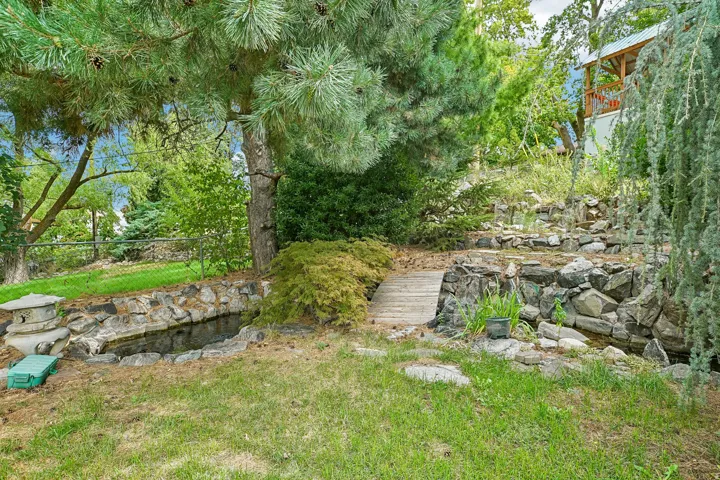 Manicured lawn with a stone-lined water feature, a small wooden bridge, and mature evergreen trees