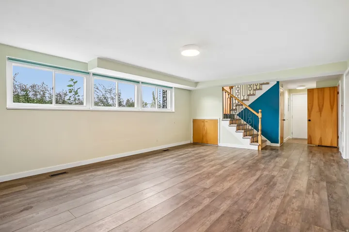 Spacious room featuring wood-finish flooring, a long window bank, a staircase with wood railings, a built-in wood-finish cabinet, and flush-mount ceiling lighting