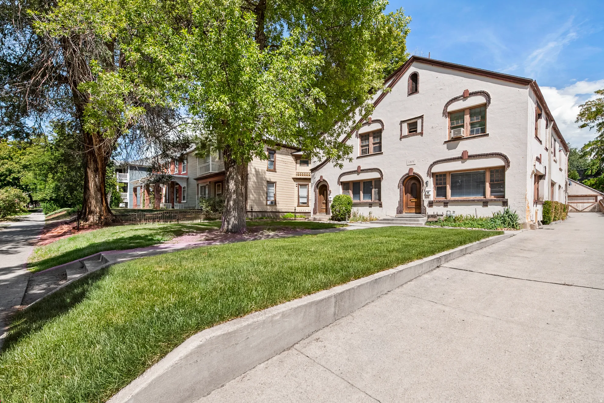 Stucco exterior with decorative window trim, arched entryway, concrete driveway, and a manicured lawn