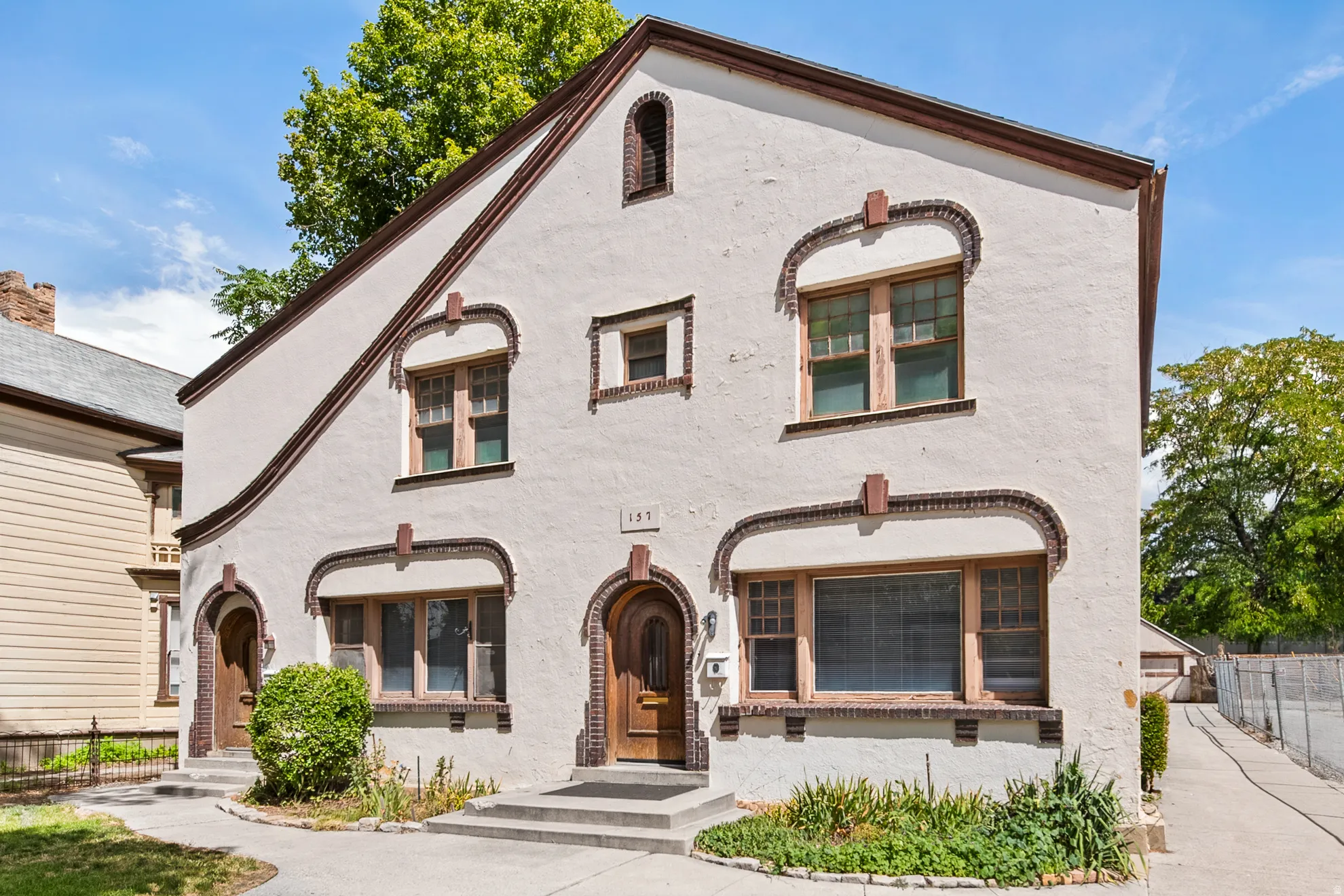 Stucco exterior with brick detailing, arched entryways, multiple window configurations, and an asphalt driveway