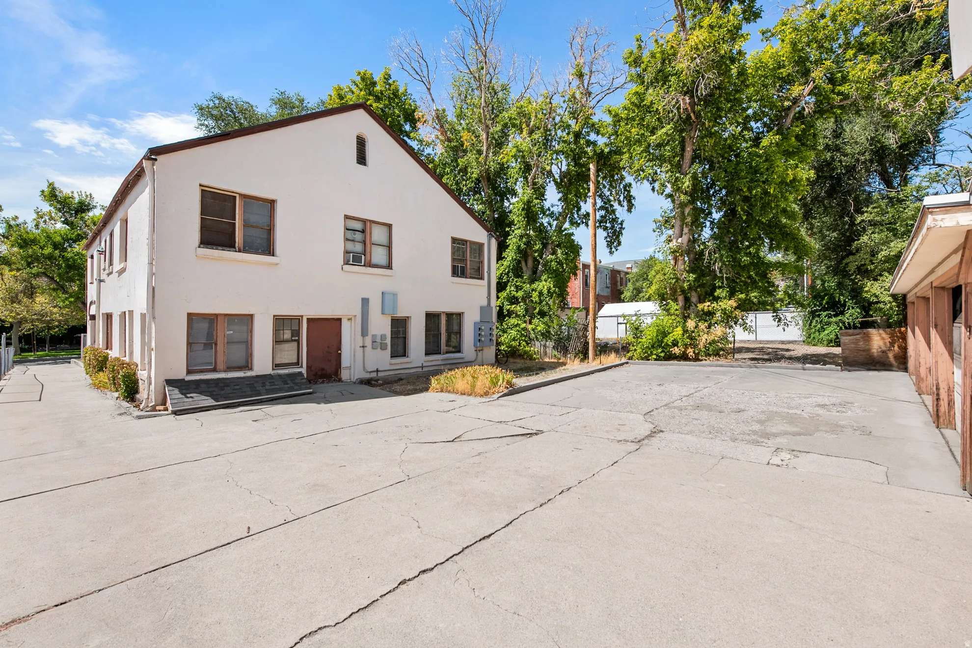 Two-story stucco exterior with multiple window units, a side entrance, and a paved parking area