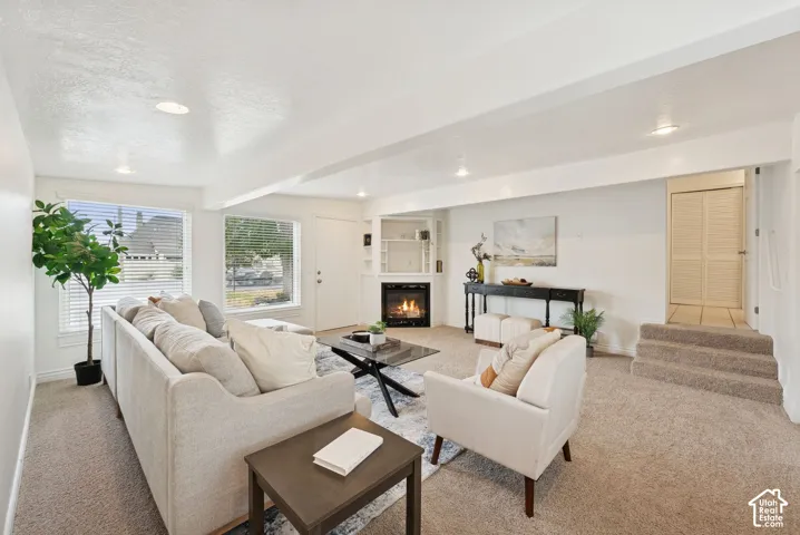 Carpeted living area featuring a corner fireplace with built-in shelving, recessed lighting, and multiple windows