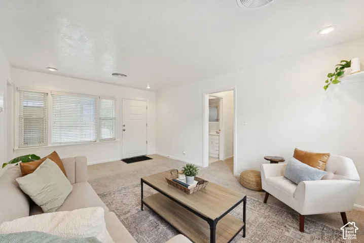 Recessed lighting illuminates the living area, featuring a front entry door with privacy blinds and a window bank