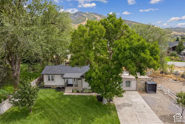 Mature landscaping, expansive lawn, mountain backdrop, paved driveway, stone facade elements