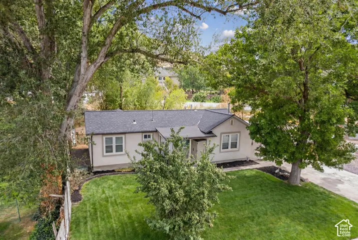 Manicured front lawn, mature trees, dark shingle roof, light-colored exterior siding, and white-framed windows