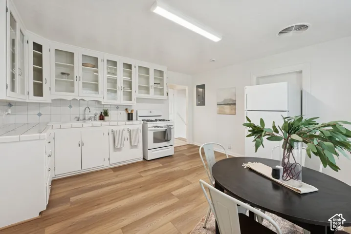 White cabinetry with glass-front uppers, tile countertops, and a tile backsplash with accent inserts
