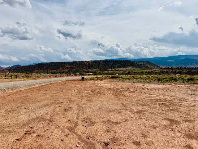 Expansive undeveloped land featuring a gravel road, split-rail fencing, and distant mountainous terrain
