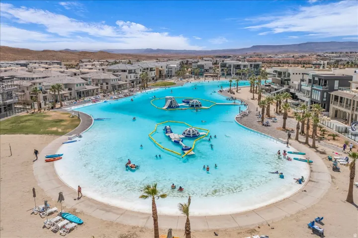 Expansive lagoon with sandy beaches, surrounding paved paths, and mature palm trees