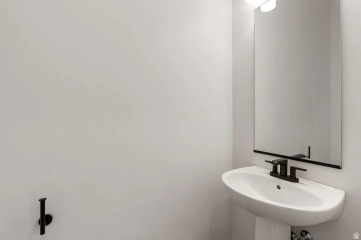 Pedestal sink with a matte black faucet, wall-mounted rectangular mirror, and overhead light fixture