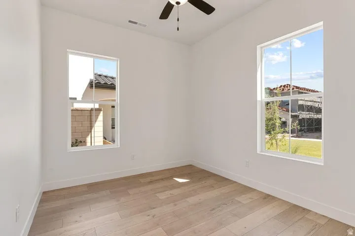 Wood-finish flooring with white baseboards, a ceiling fan, and multiple windows