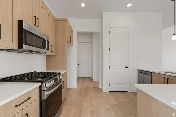 Contemporary kitchen featuring light wood-finish cabinetry, stainless steel appliances, white countertops, and a white subway tile backsplash