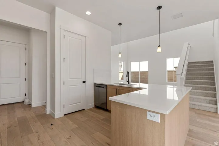 Open-concept kitchen featuring an island with a light-toned countertop, wood-finish flooring, white subway tile backsplash, and stainless steel dishwasher