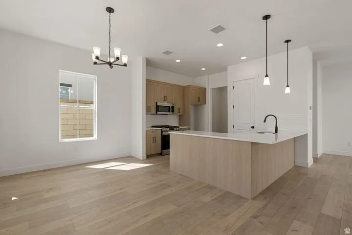 Open-concept living space featuring wood-finish flooring, a kitchen island with a sink and pendant lighting, light-toned cabinetry, and a range with a microwave