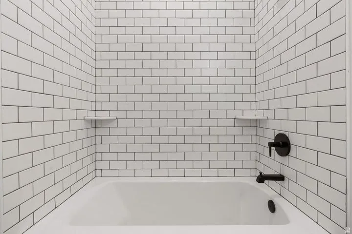 Bathtub with subway tile surround, integrated shelving, and matte black fixtures