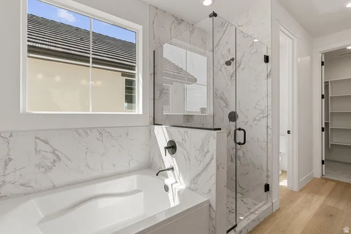 Soaking tub with wall-mounted faucet, marble-finish tile surround, and frameless glass shower enclosure with dark fixtures