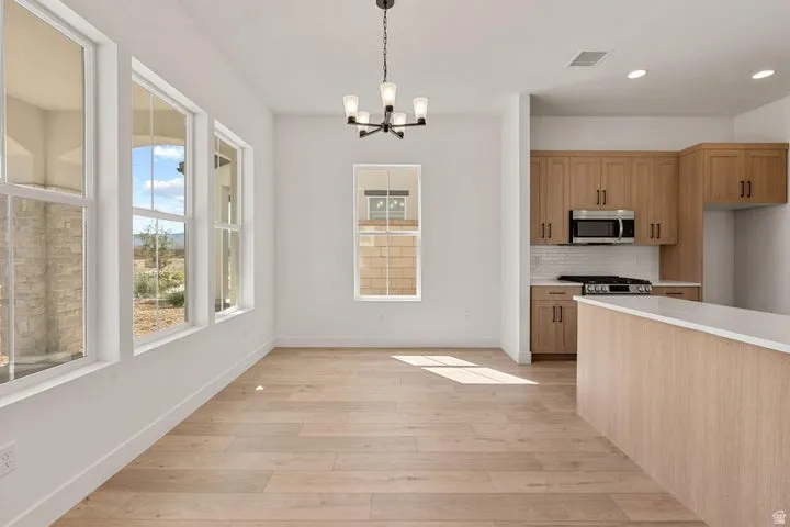 Wood-finish flooring, multiple windows, kitchen with light wood-tone cabinetry, white subway tile backsplash, and stainless steel appliances