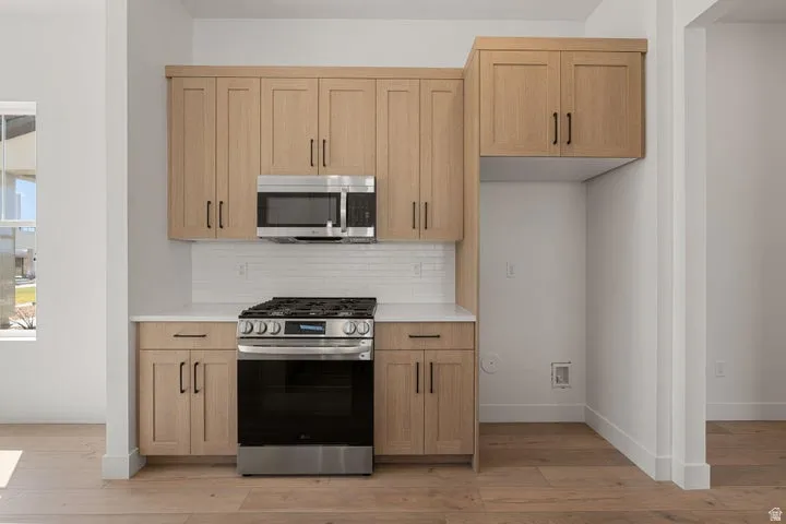 Modern kitchen featuring light wood-finish cabinetry, stainless steel microwave, gas range, white subway tile backsplash, and light wood-finish flooring