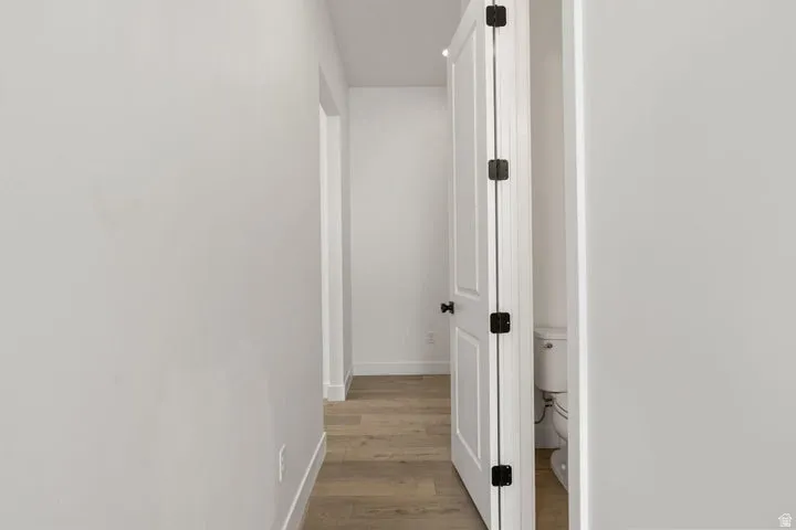 Wood-finish flooring with white wall finishes and a white paneled door featuring black hardware