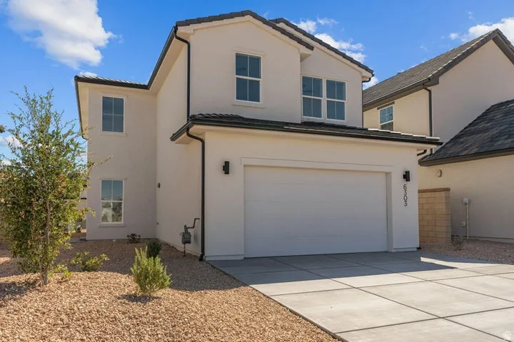 Contemporary stucco exterior with a two-car garage, concrete driveway, dark roof tiles, and minimalist landscaping